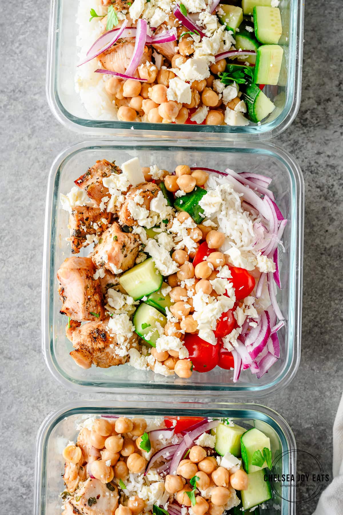 Overhead view of chicken souvlaki bowls divided in bowls for meal prep, with rice, fresh veggies, chickpeas, and feta cheese