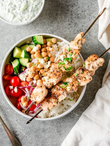 Overhead view of chicken souvlaki bowls with chicken skewers, rice, and fresh veggies