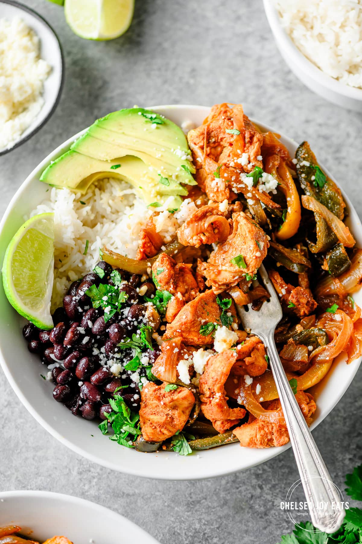 Closeup of a fajita chicken bowl with bell peppers, onions, rice, black beans, and avocado with a fork in the bowl