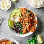 Overhead view of a bowl filled with fajita chicken, sauted peppers and onions, black beans, rice, and avocado, topped with cotija cheese and cilantro