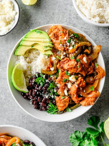 Overhead view of a bowl filled with fajita chicken, sauted peppers and onions, black beans, rice, and avocado, topped with cotija cheese and cilantro