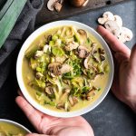 Hands holding a bowl of mushroom, leek, and chicken soup