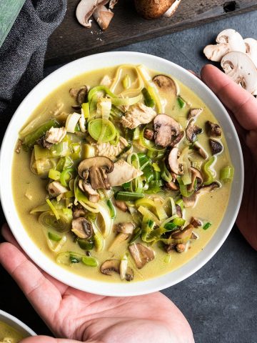 Hands holding a bowl of mushroom, leek, and chicken soup