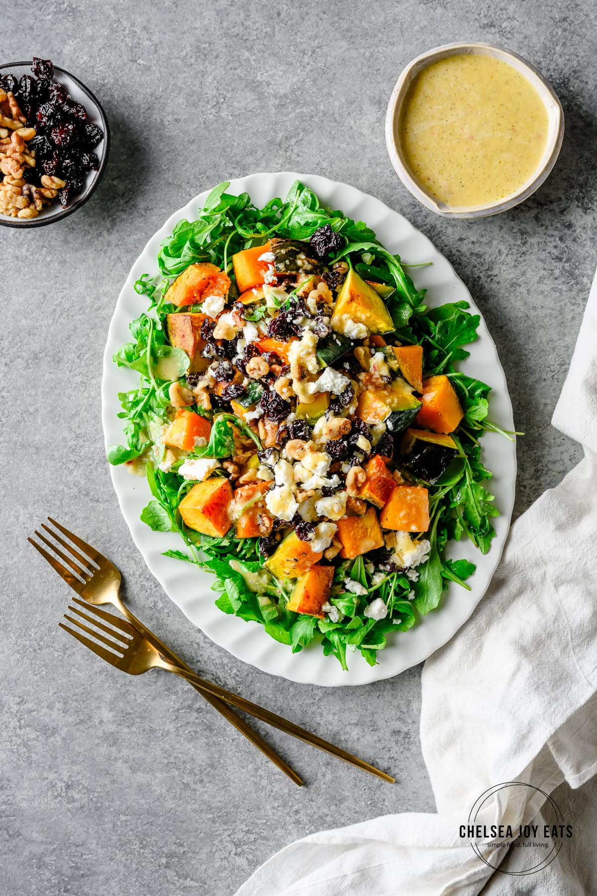 Overhead view of an arugula and roasted squash salad topped with toasted walnuts, dried cherries, and feta cheese along with a honey vanilla vinaigrette