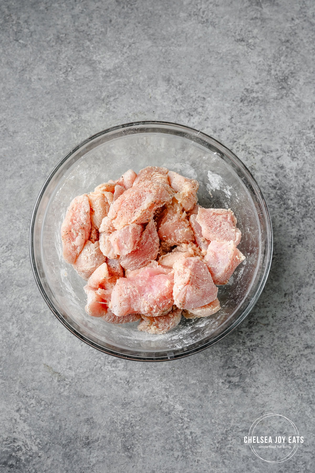 Chicken pieces tossed with flour and spices in a bowl