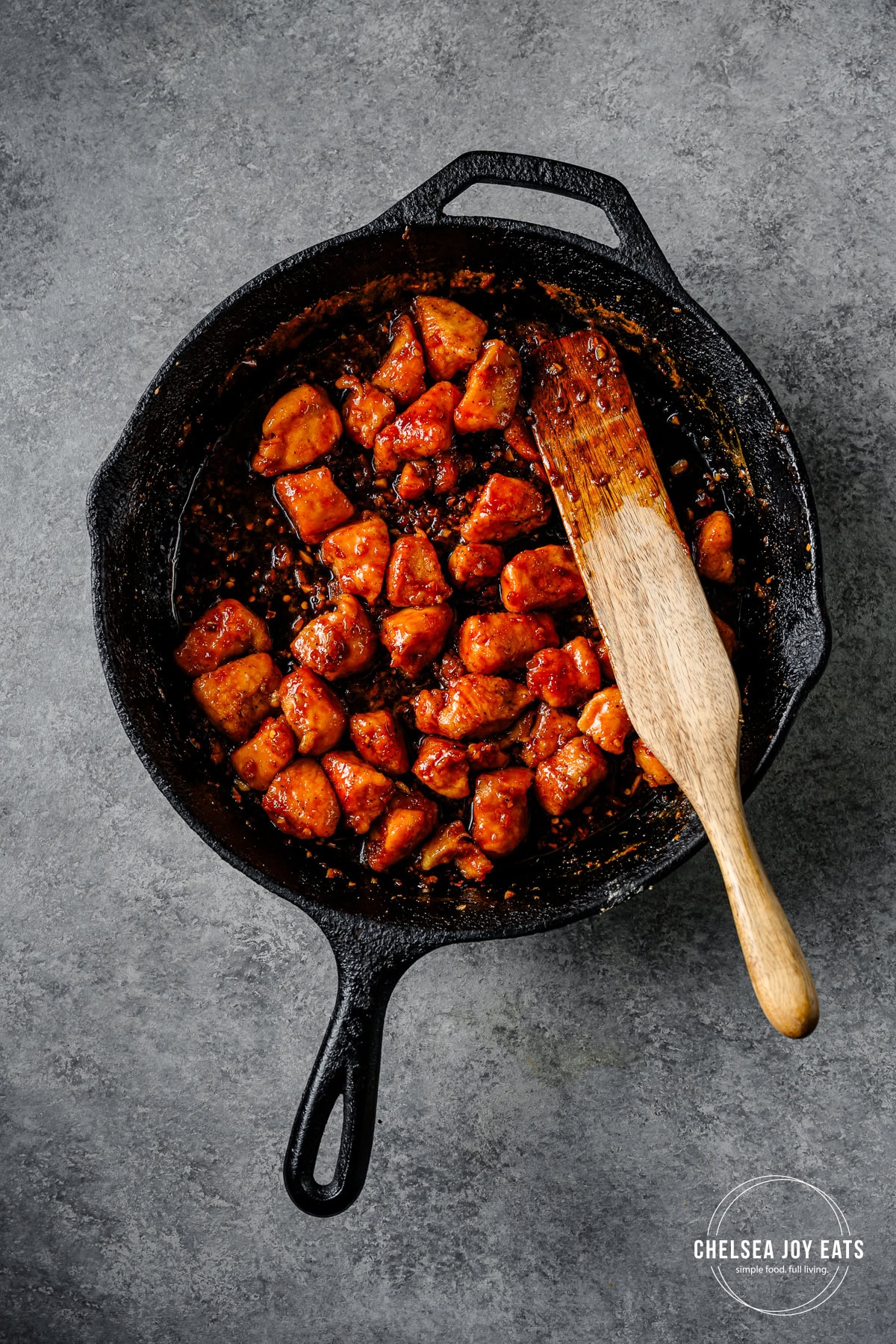 Finished honey garlic chicken in a cast iron skillet with a spurdle stirring the mixture
