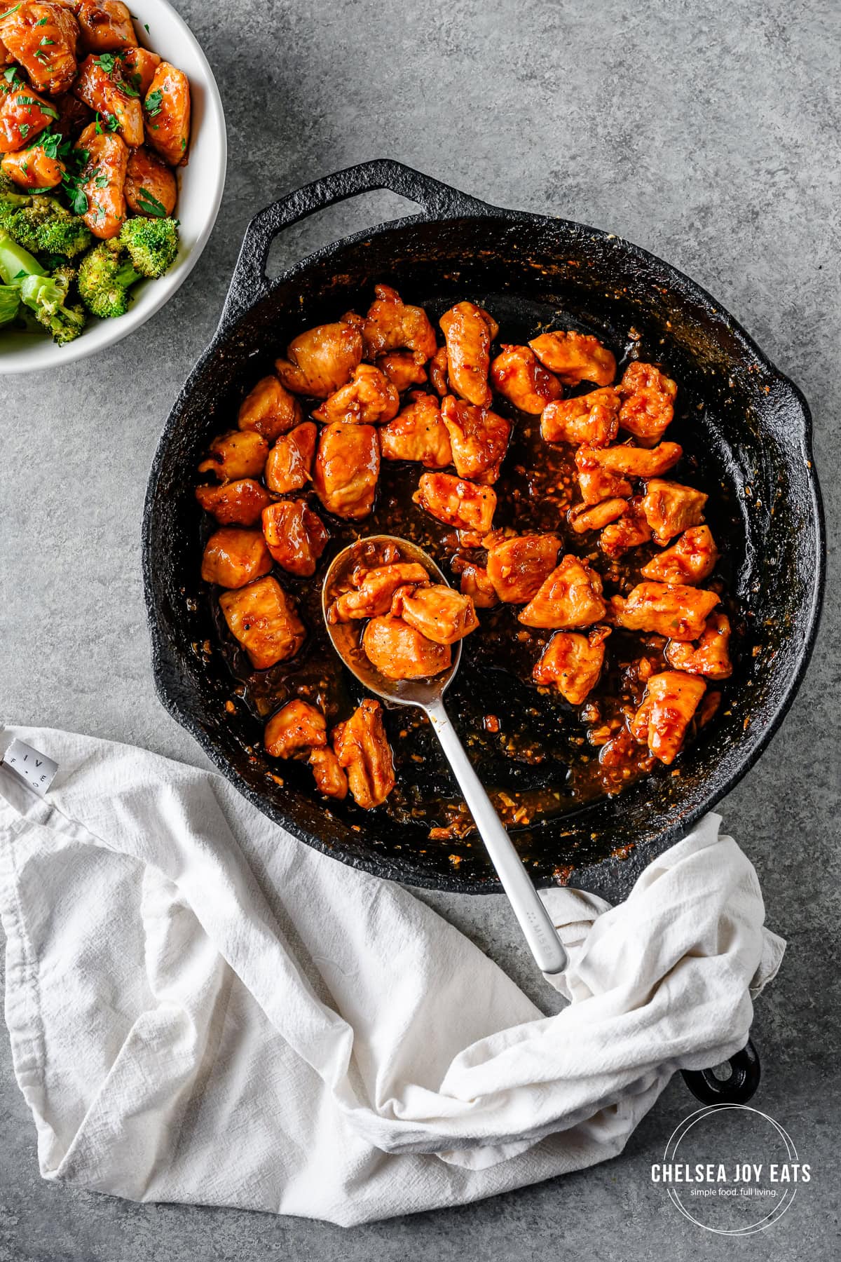 Honey garlic chicken in a skillet with a metal serving spoon ready to scoop the chicken into bowls.