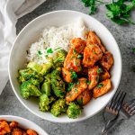 Overhead view of a bowl with rice, roasted broccoli, and gluten free honey garlic chicken garnished with parsley