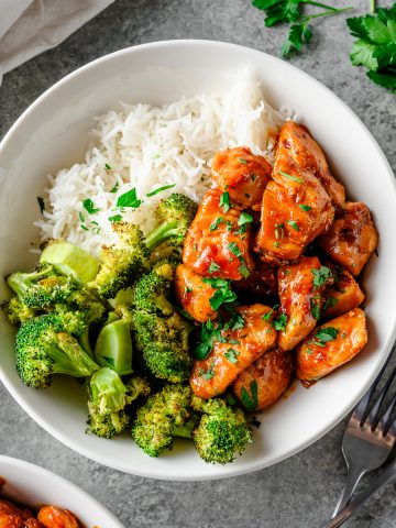 Overhead view of a bowl with rice, roasted broccoli, and gluten free honey garlic chicken garnished with parsley