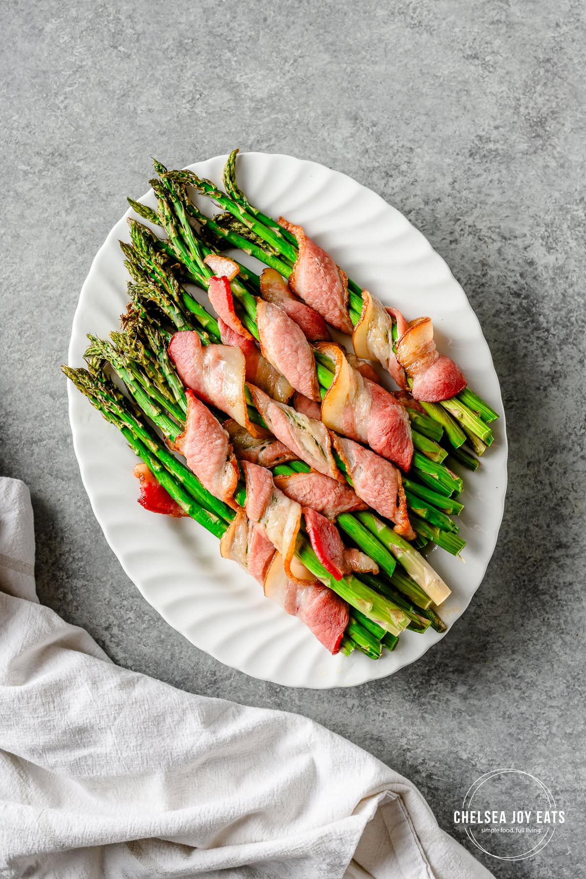 Bundles of bacon-wrapped roasted asparagus on a white ceramic platter.