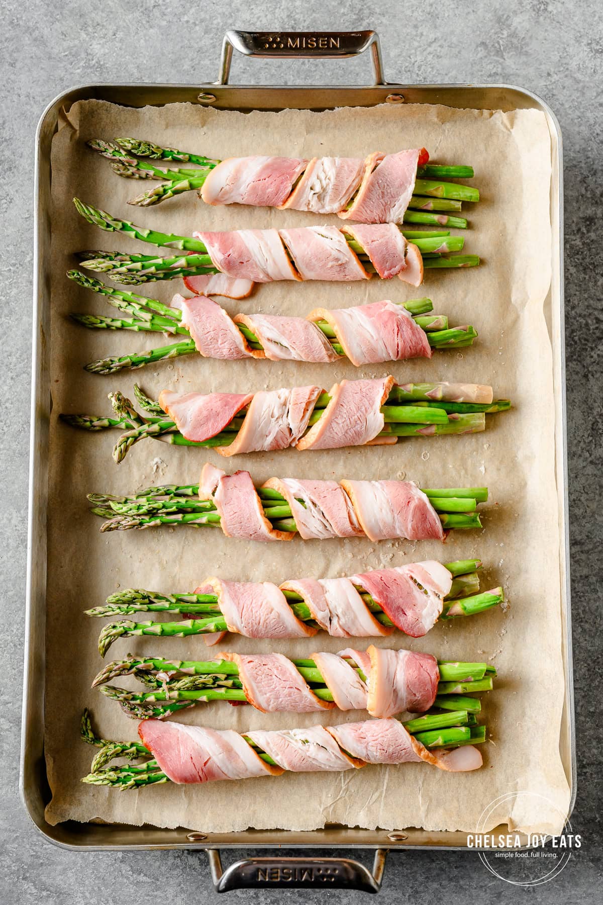 Bundles of bacon-wrapped asparagus on a parchment paper lined baking sheet.