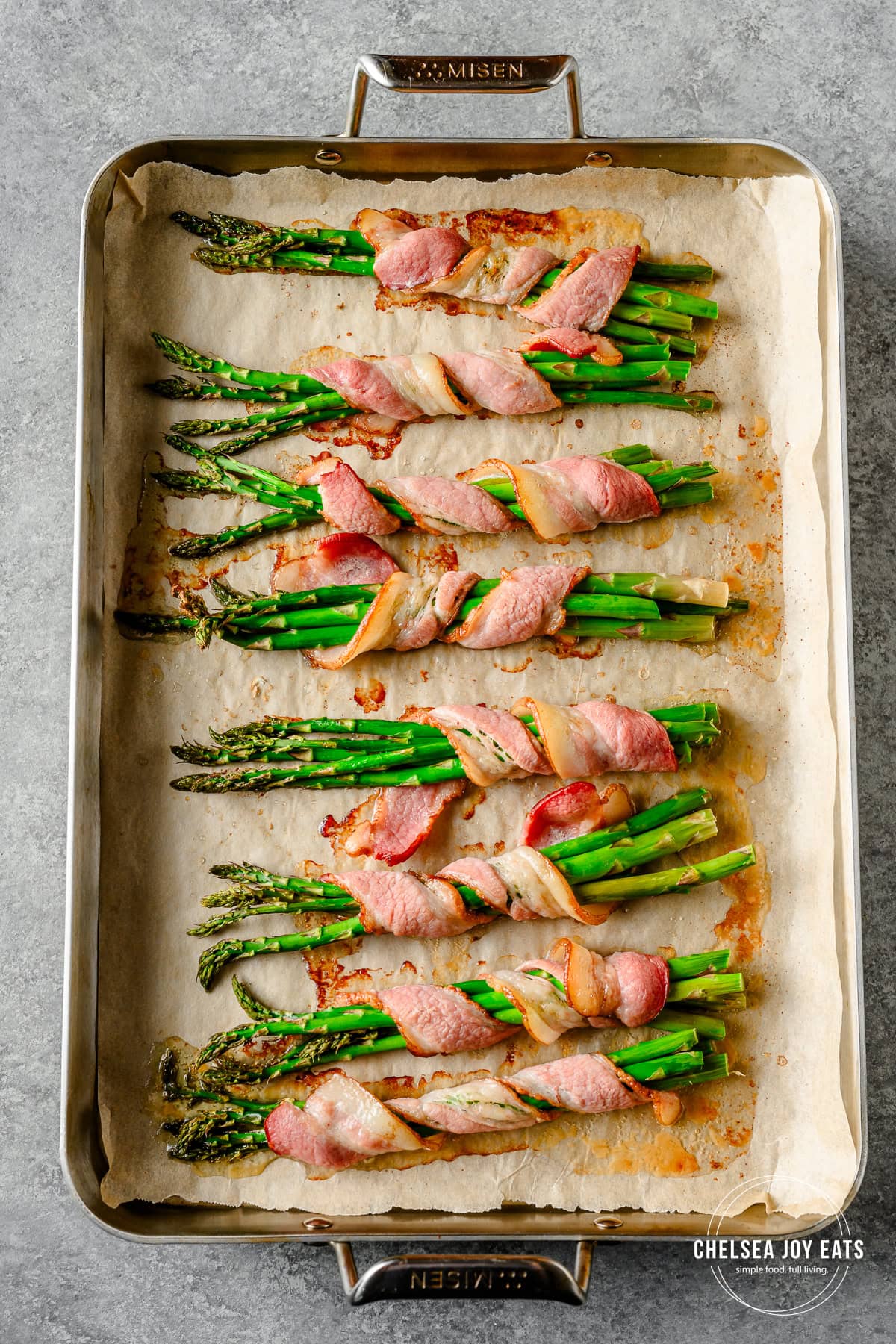 Bundles of oven-roasted bacon-wrapped asparagus on a parchment paper lined baking sheet.