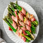 Bacon-wrapped roasted asparagus bundles on a white ceramic platter.