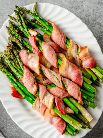 Bacon-wrapped roasted asparagus bundles on a white ceramic platter.