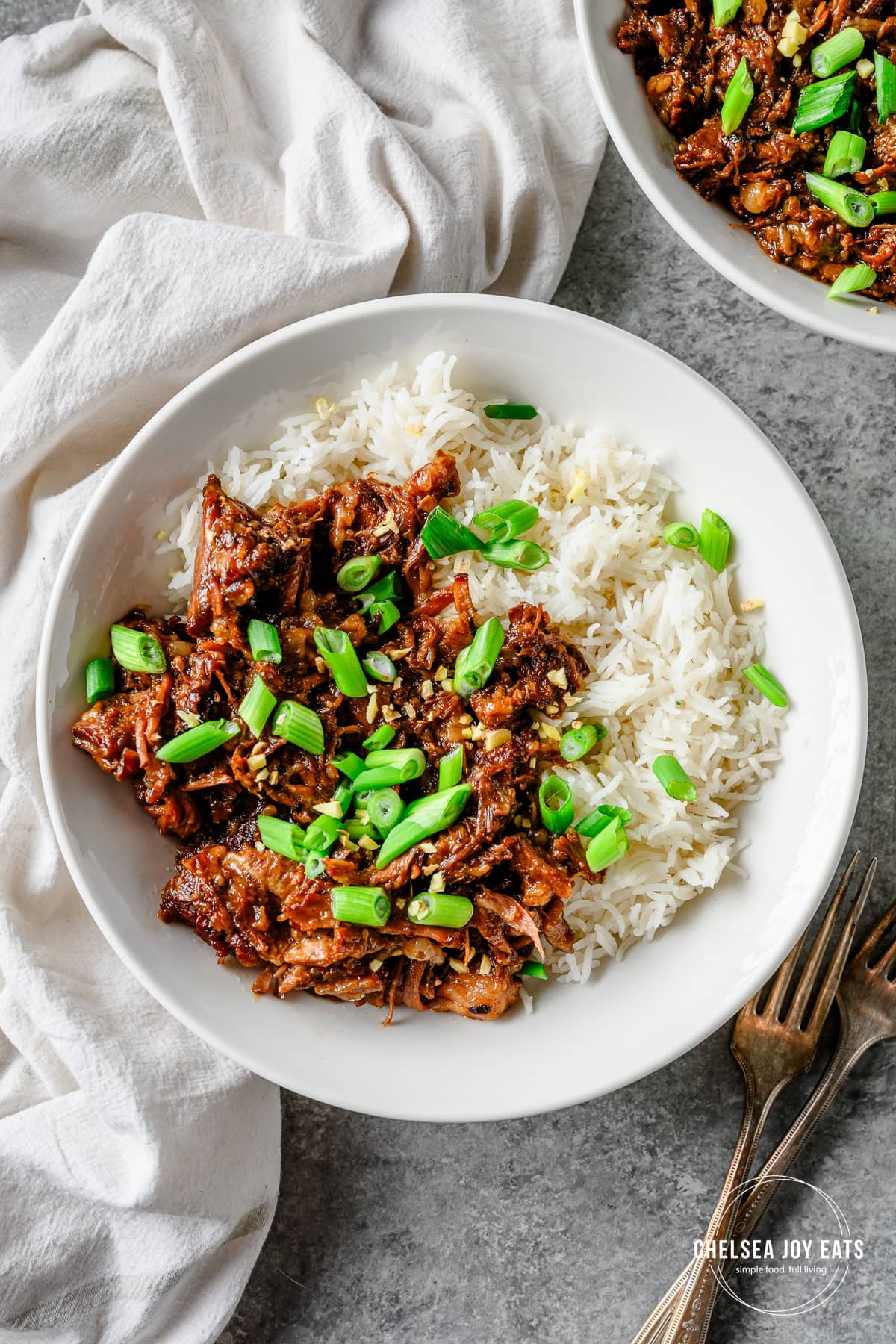 White bowl with a serving of rice and shredded braised ginger scallion short ribs garnished with sliced scallions.