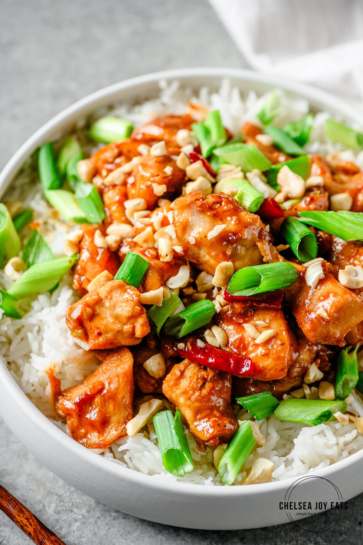 Gluten free Kung Pao chicken with toasted cashews, Szechuan peppers, and sliced scallions served over rice in a bowl.