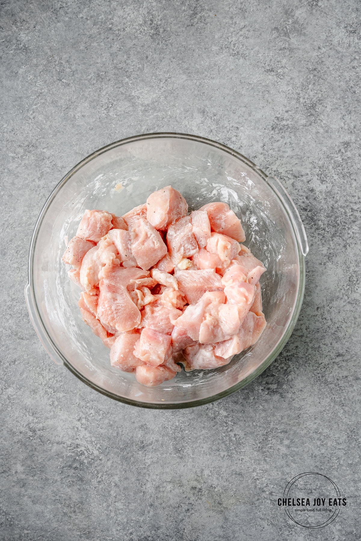 Glass bowl with pieces of chicken breast tossed with arrowroot flour.
