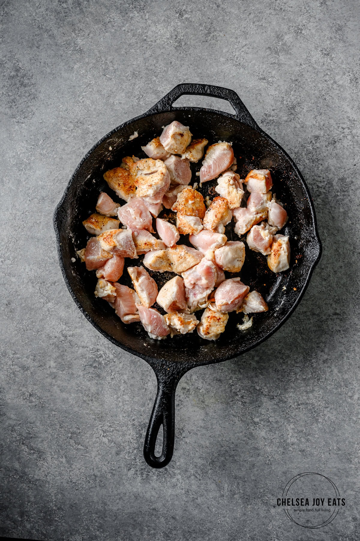 Cast iron skillet with chicken pieces browning in oil.