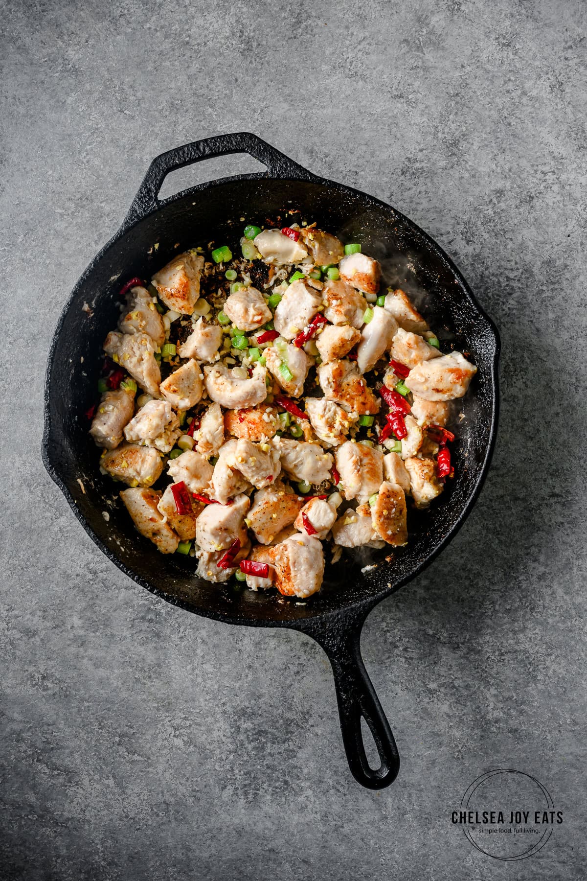 Cast iron skillet with chicken, garlic, ginger, scallions, and dried arbol chiles cooking.