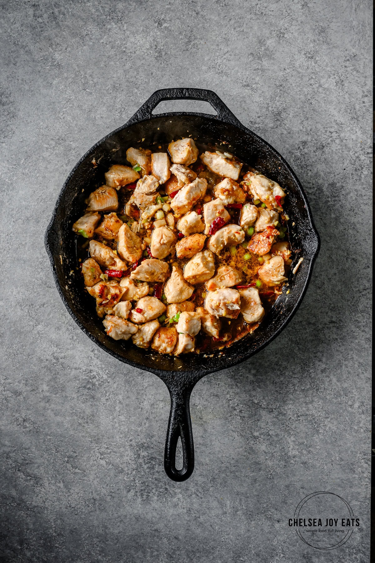 Cast iron skillet with chicken breast and sauce for kung pao chicken simmering.