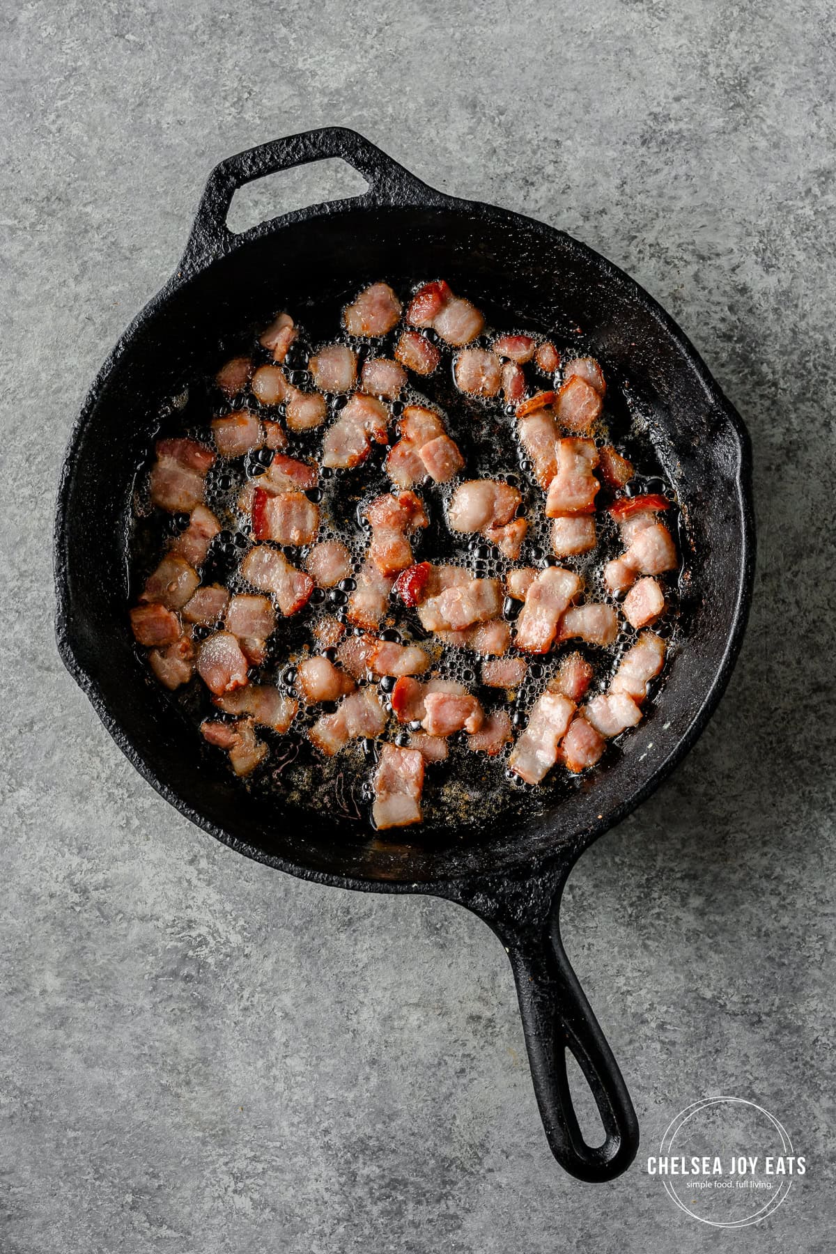Bacon pieces frying in a cast iron skillet.
