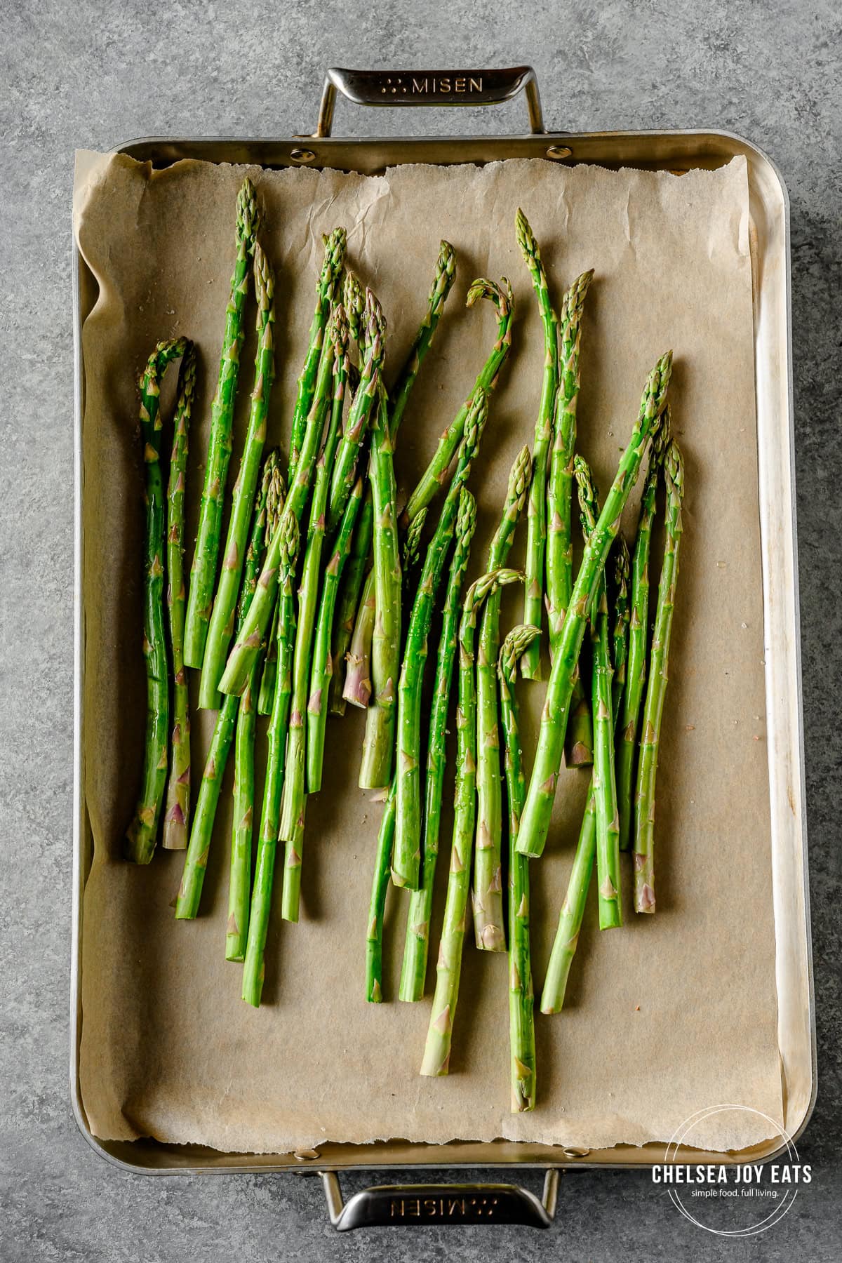 Roasted asparagus on a stainless steel baking sheet lined with parchment paper.