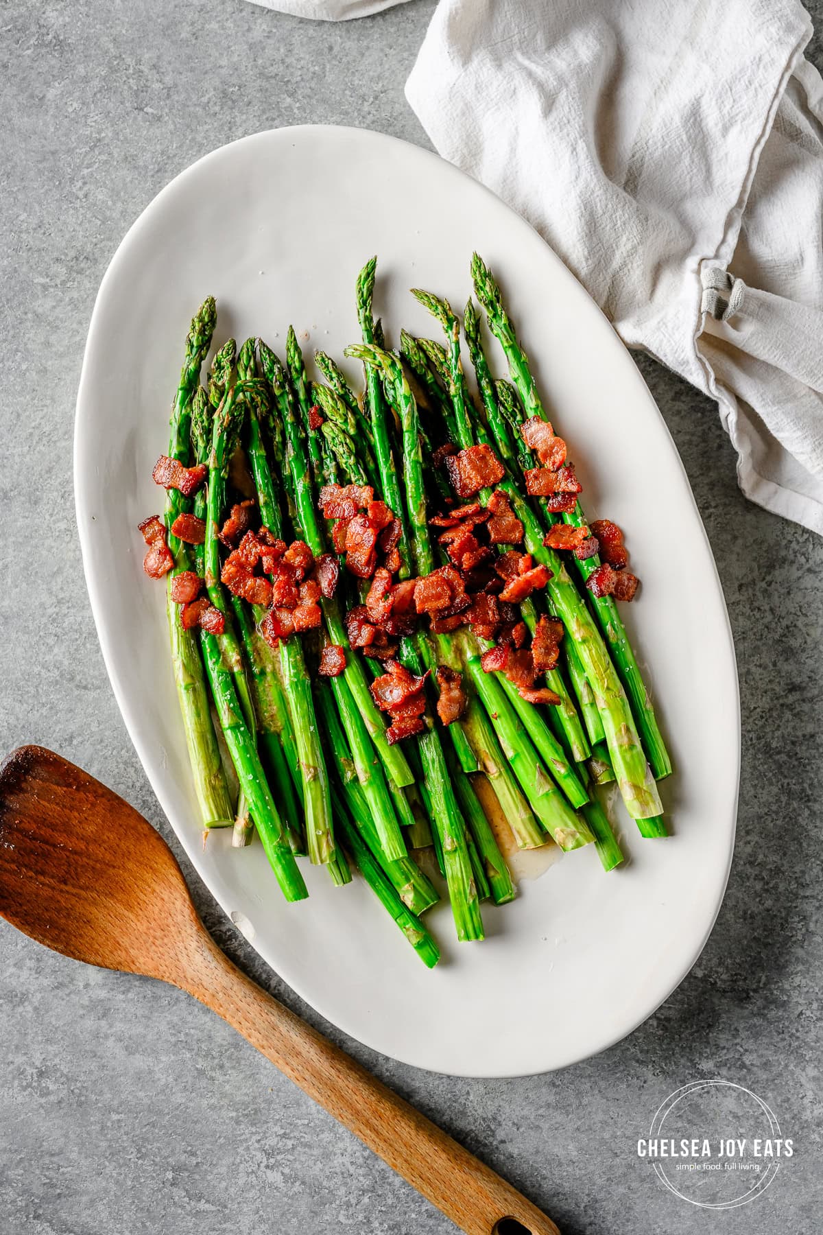 Roasted asparagus topped with maple bacon vinaigrette and crispy bacon pieces on a white serving platter.