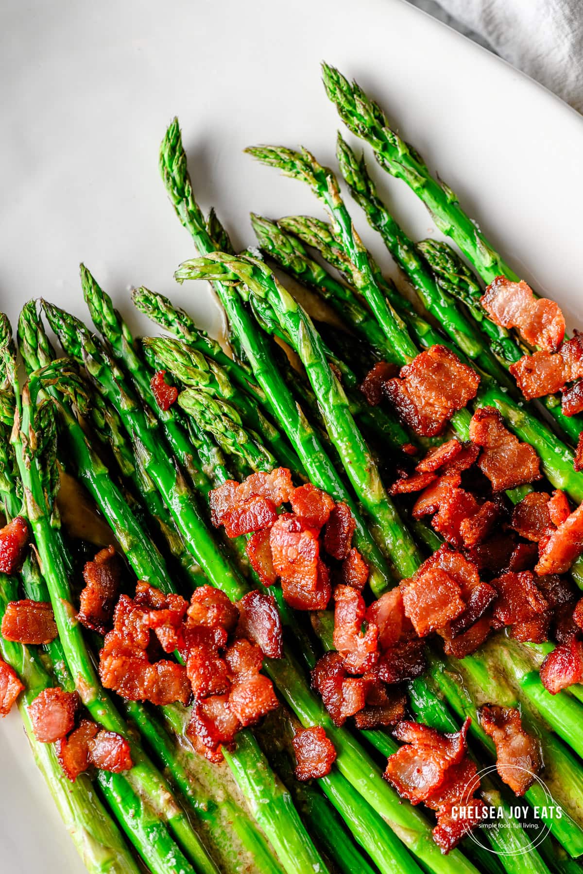 Roasted asparagus drizzled in maple bacon vinaigrette and topped with crispy bacon pieces on a white ceramic platter.