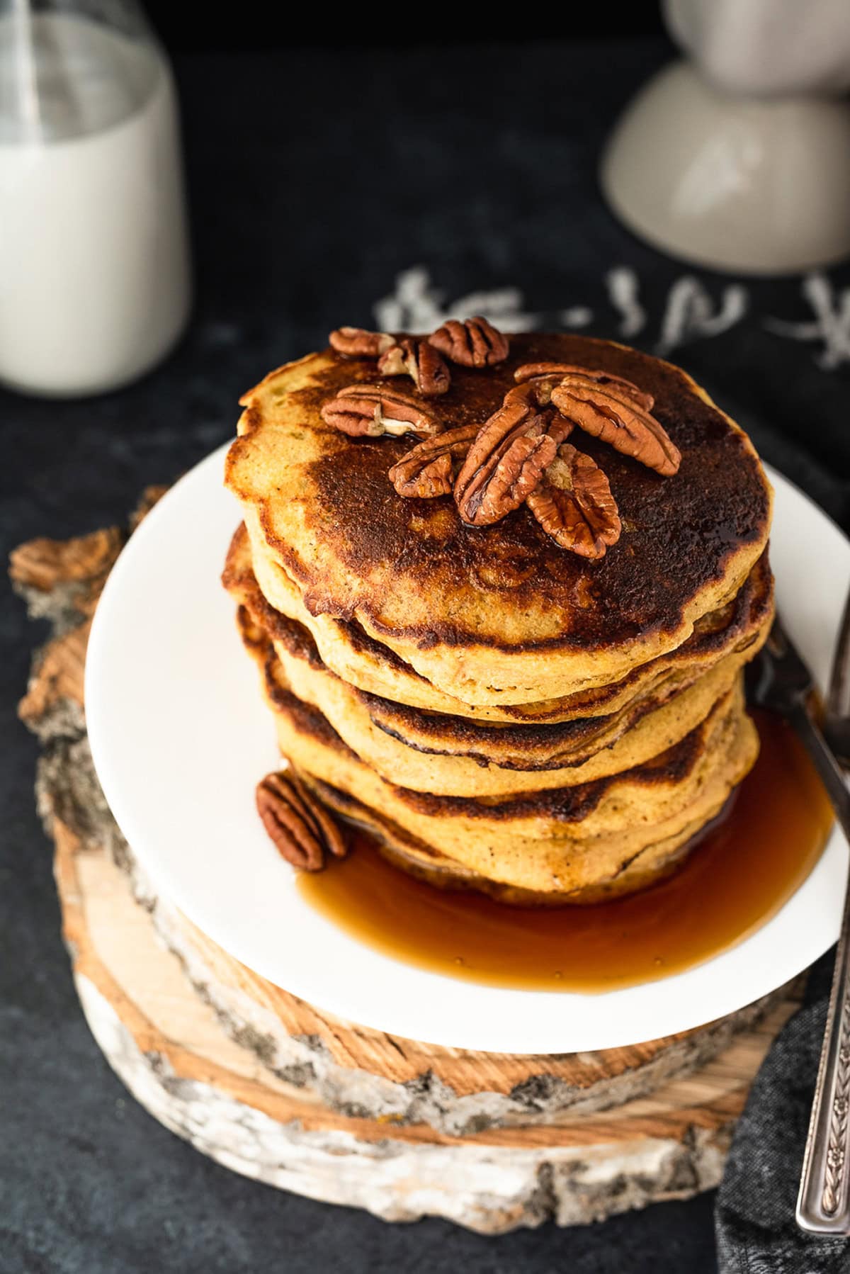 Stack of pancakes topped with pecans and maple syrup served on a white plate.