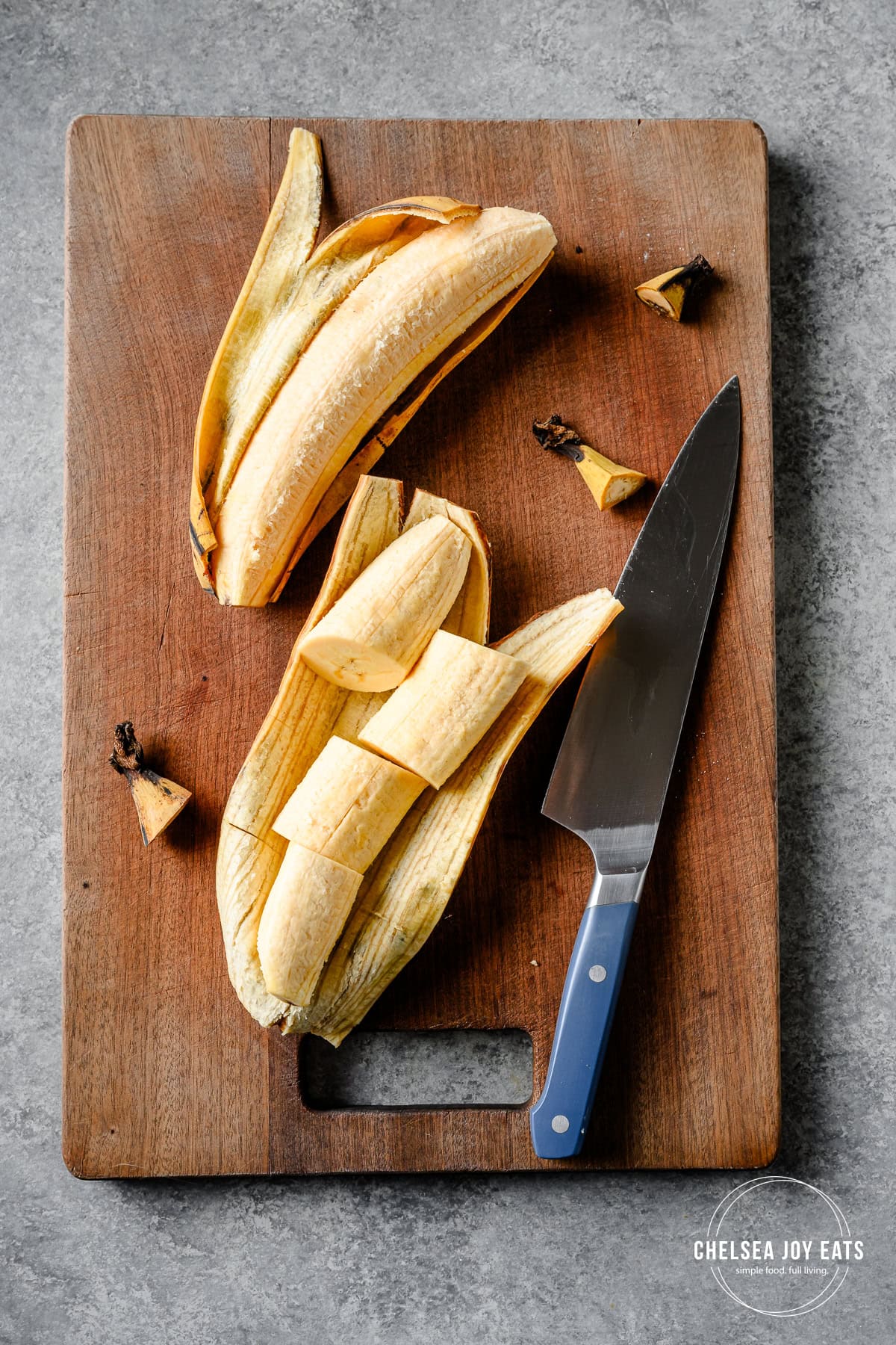 Two peeled yellow plantains on a cutting board, one sliced, with a knife alongside.