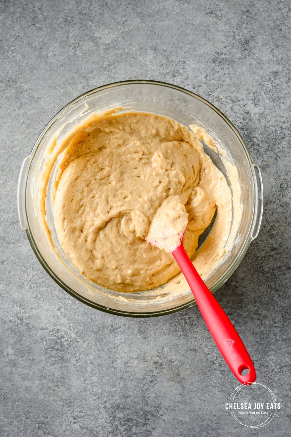 Batter for gluten free plantain pancakes mixed in a glass bowl with a red spatula.