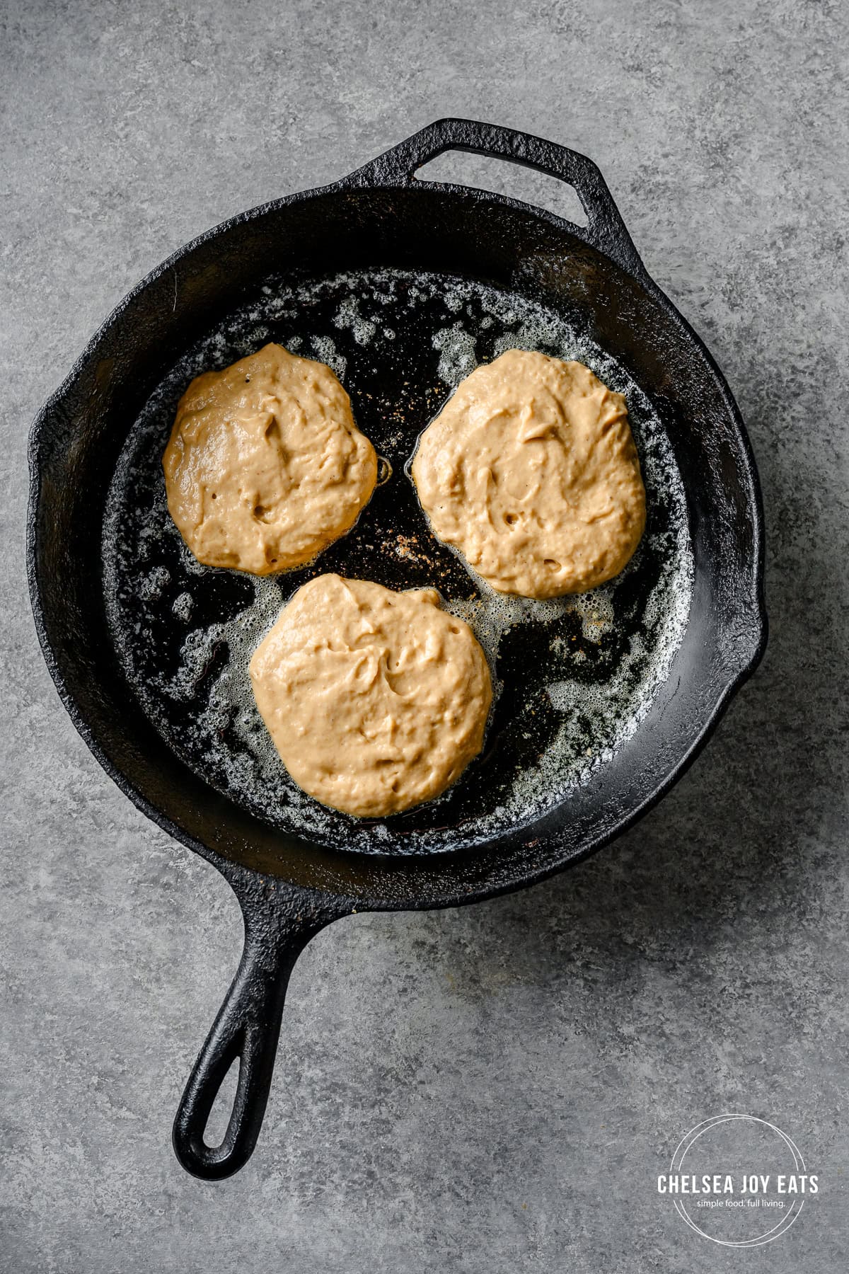 Plantain pancake batter cooking in a cast iron skillet.
