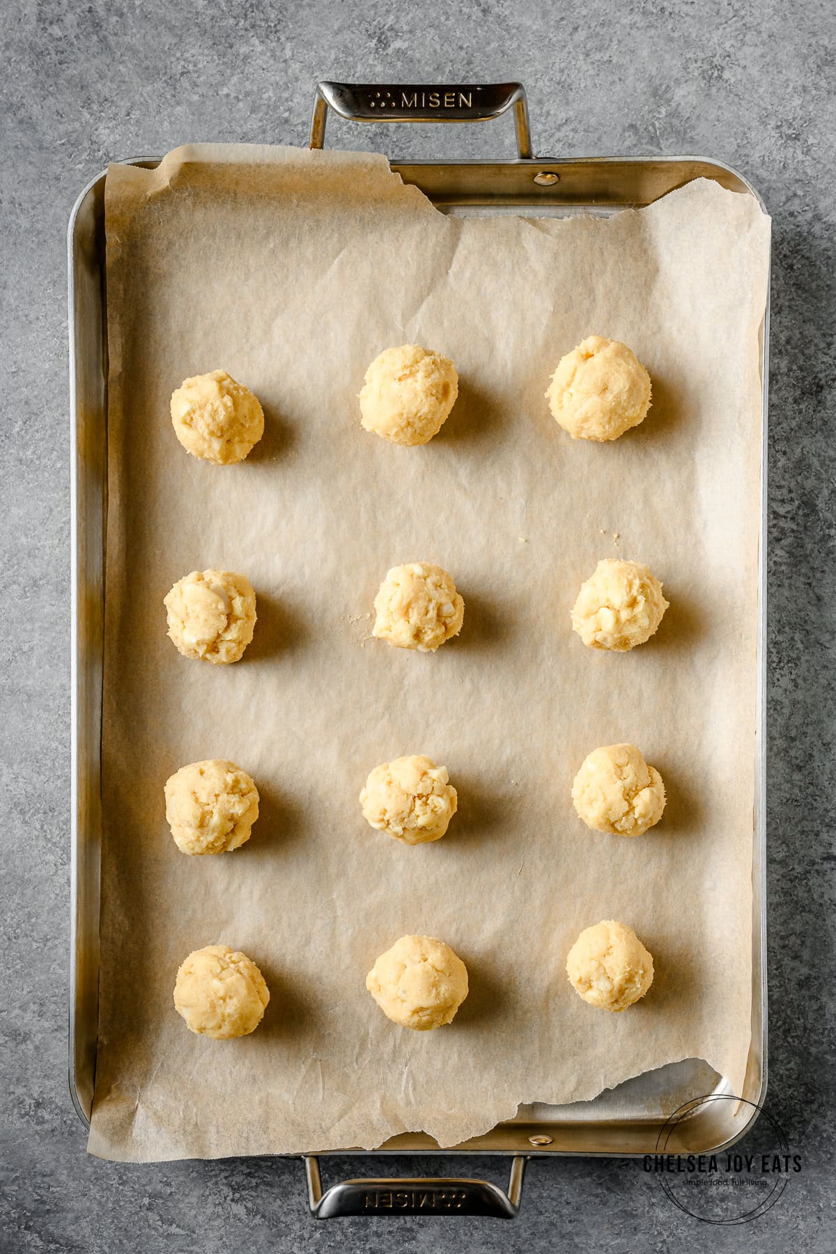 Gluten free white chocolate macadamia cookie dough balls lined on a baking sheet ready to go in the oven.
