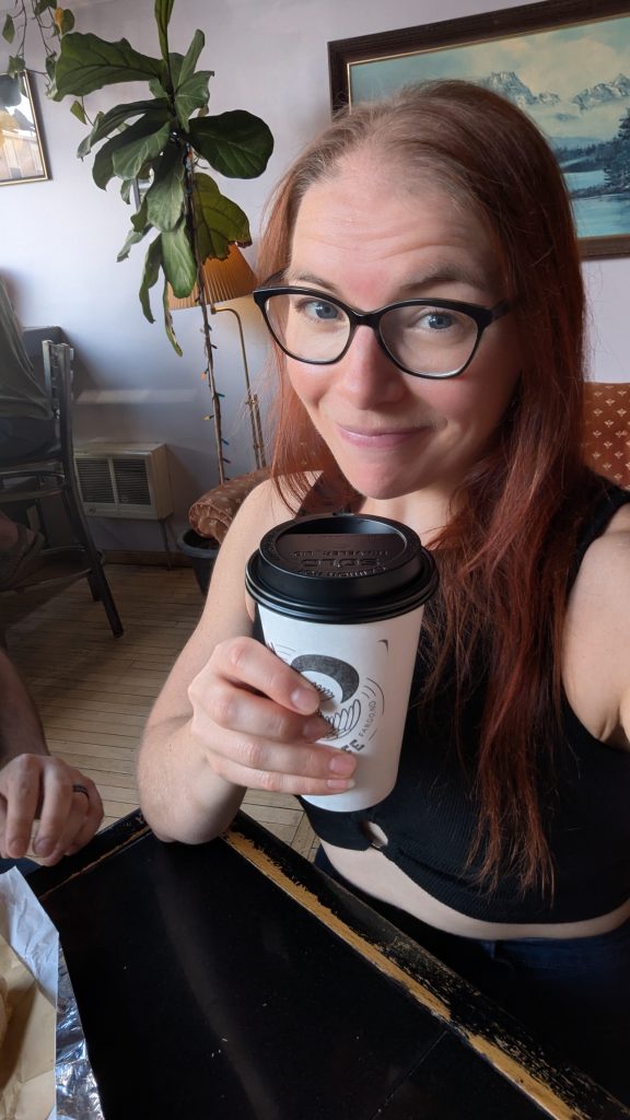 Chelsea Joy from Chelsea Joy Eats holding a cup of coffee in a coffee shop.