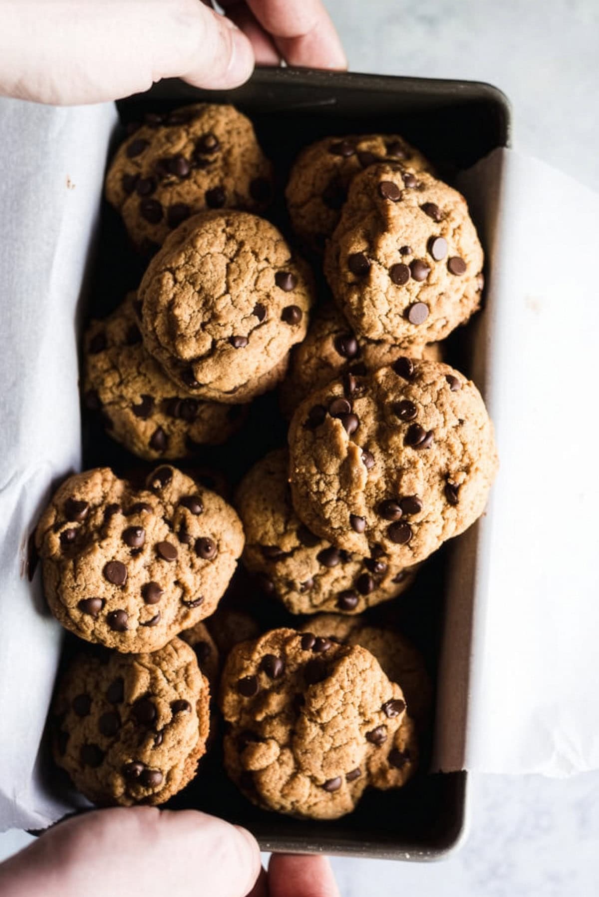 Person holidng a small tin tray with gluten free tahini chocolate chip cookies.