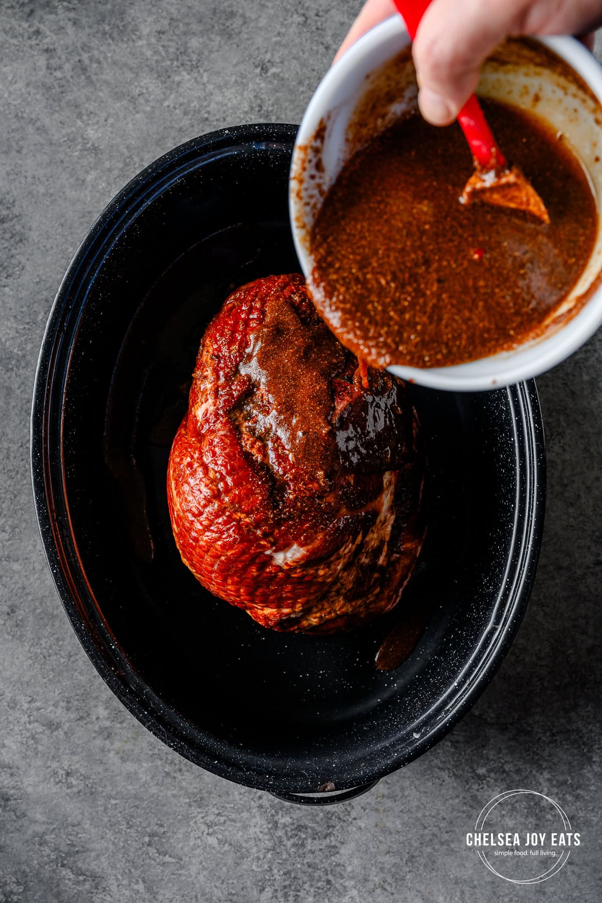 Person pouring gluten free ham glaze over a pre-cooked spiral-cut ham in a roaster pan.