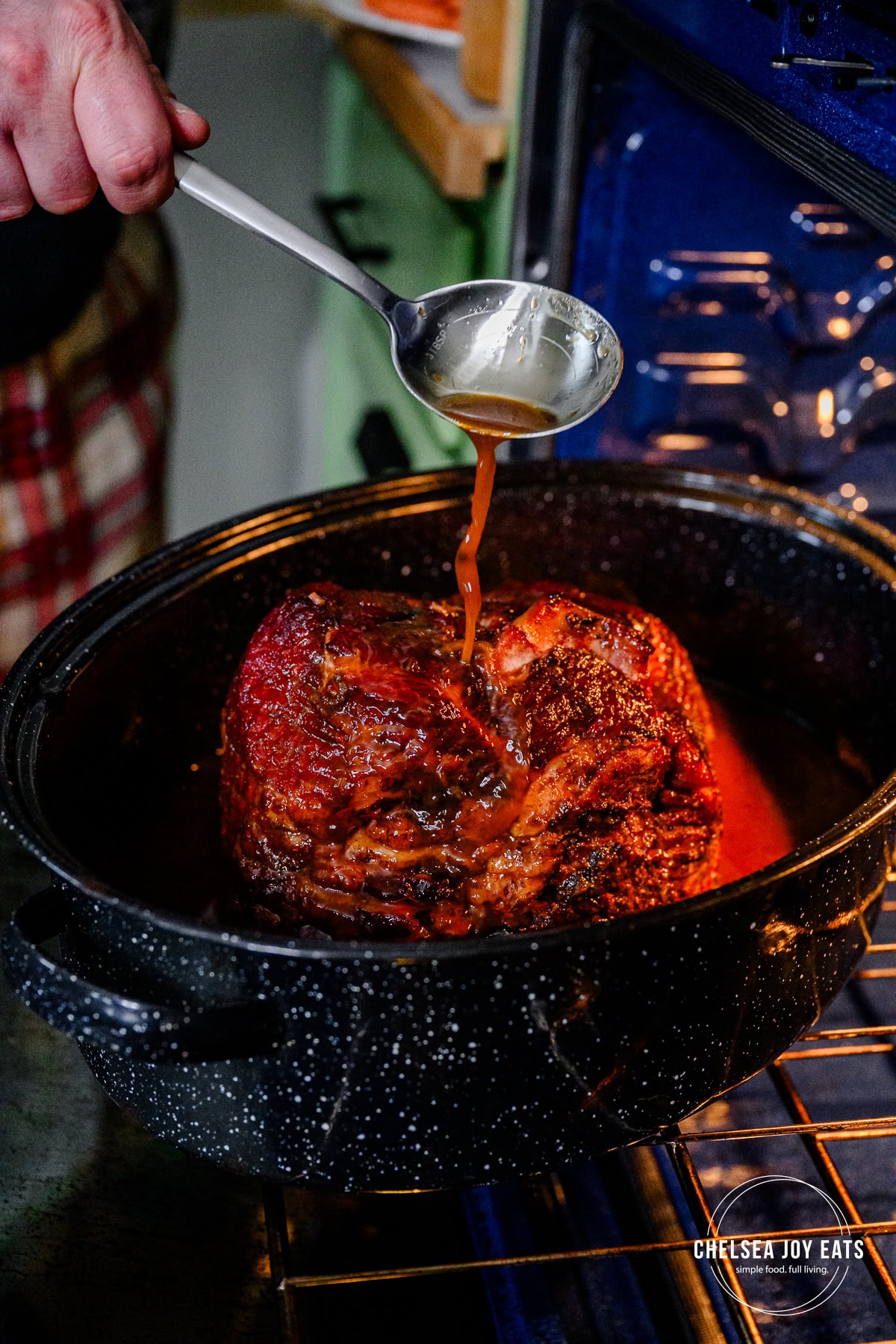 Person basting a spiral-cut ham with basting juices in a roaster pan.