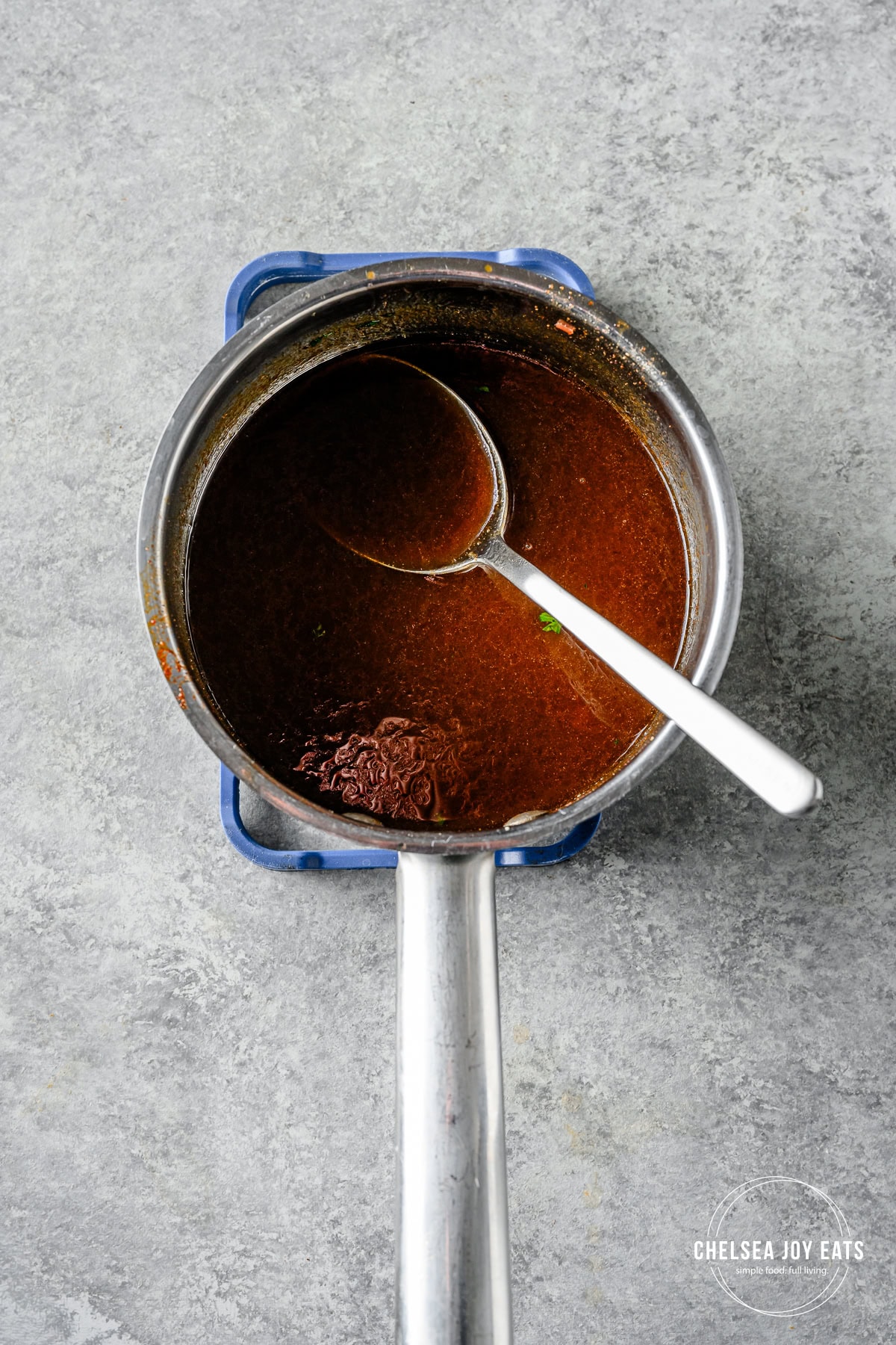 Basting juices with ham glaze in a saucepan and a metal spoon.