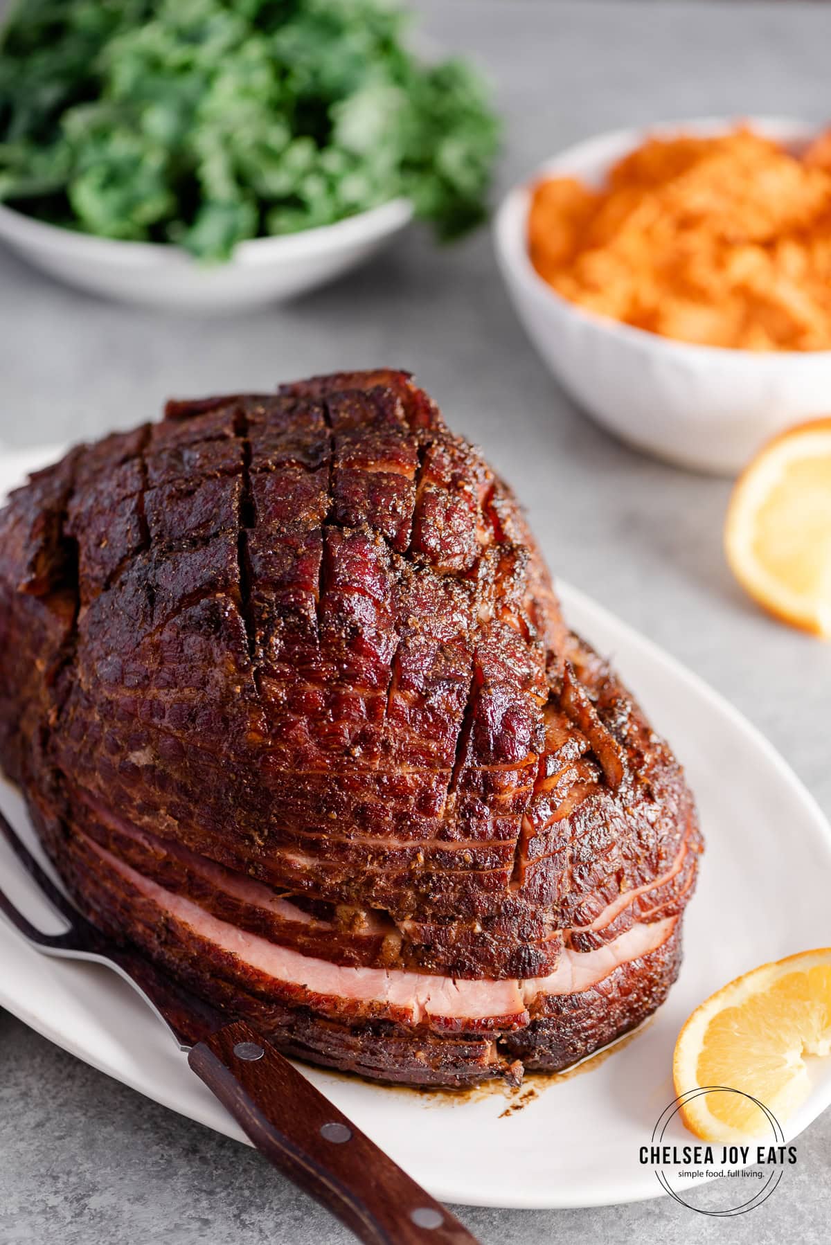 Cooked spiral cut glazed ham with side dishes in the background.