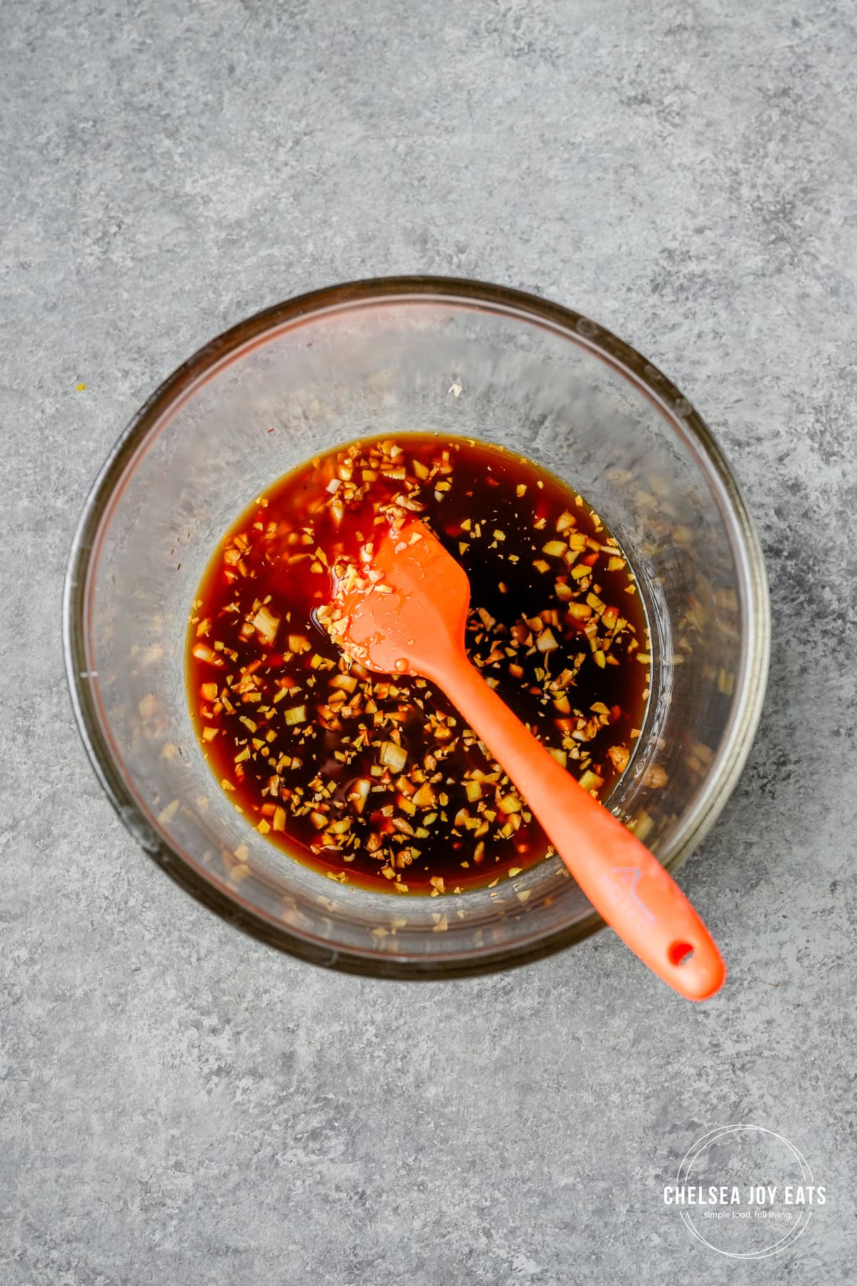 Sauce for honey sesame chicken stirred in a bowl with a silicon spatula.