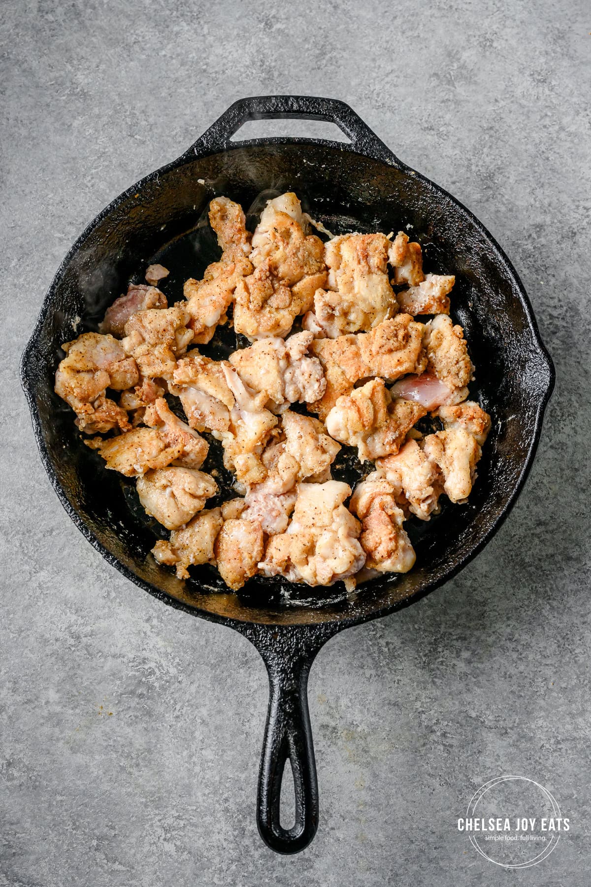 Chicken pieces pan-frying in a cast iron skillet.