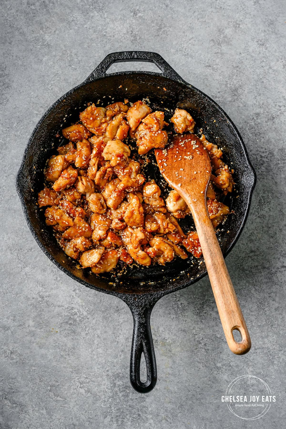 Finished gluten free honey sesame chicken stirred in a skillet with a wooden spoon.