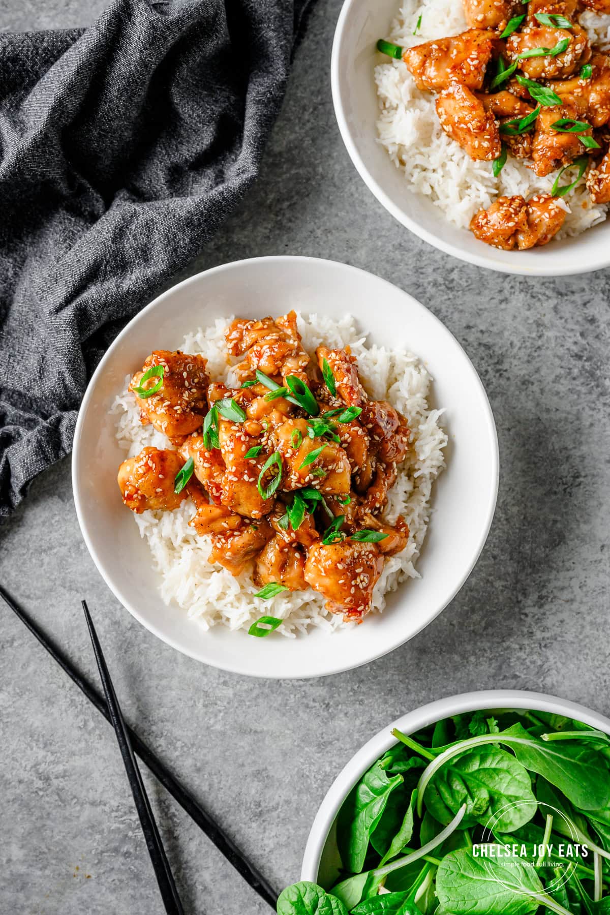 Bowls with rice and gluten free honey sesame chicken bites garnished with scallions, with chopsticks besides.