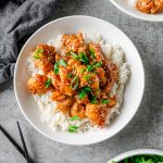 Bowl with rice and gluten free honey sesame chicken garnished with scallions.