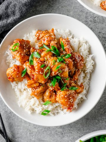 Bowl with rice and gluten free honey sesame chicken garnished with scallions.