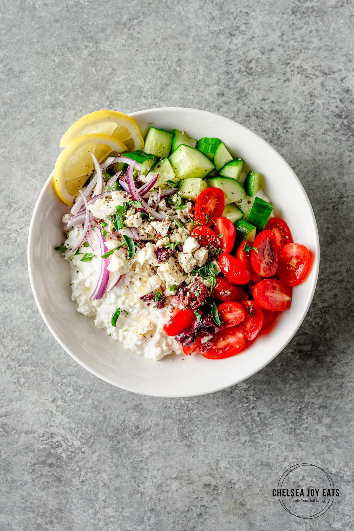 Assembled Greek cottage cheese bowls with tomatoes, olives, cucumber, red onion, and fresh herbs.