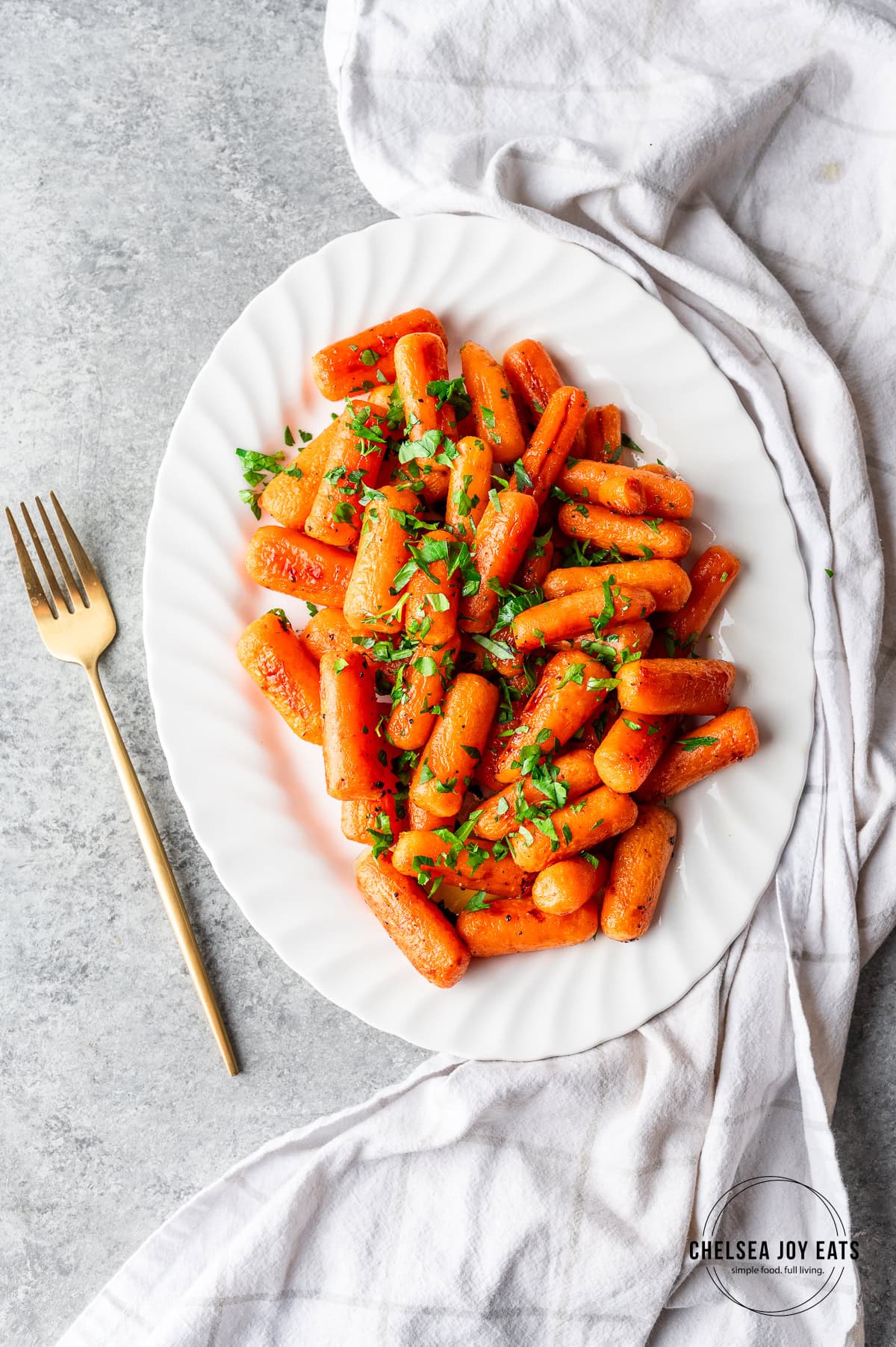 Roasted baby carrots garnished with parsley on a white platter.