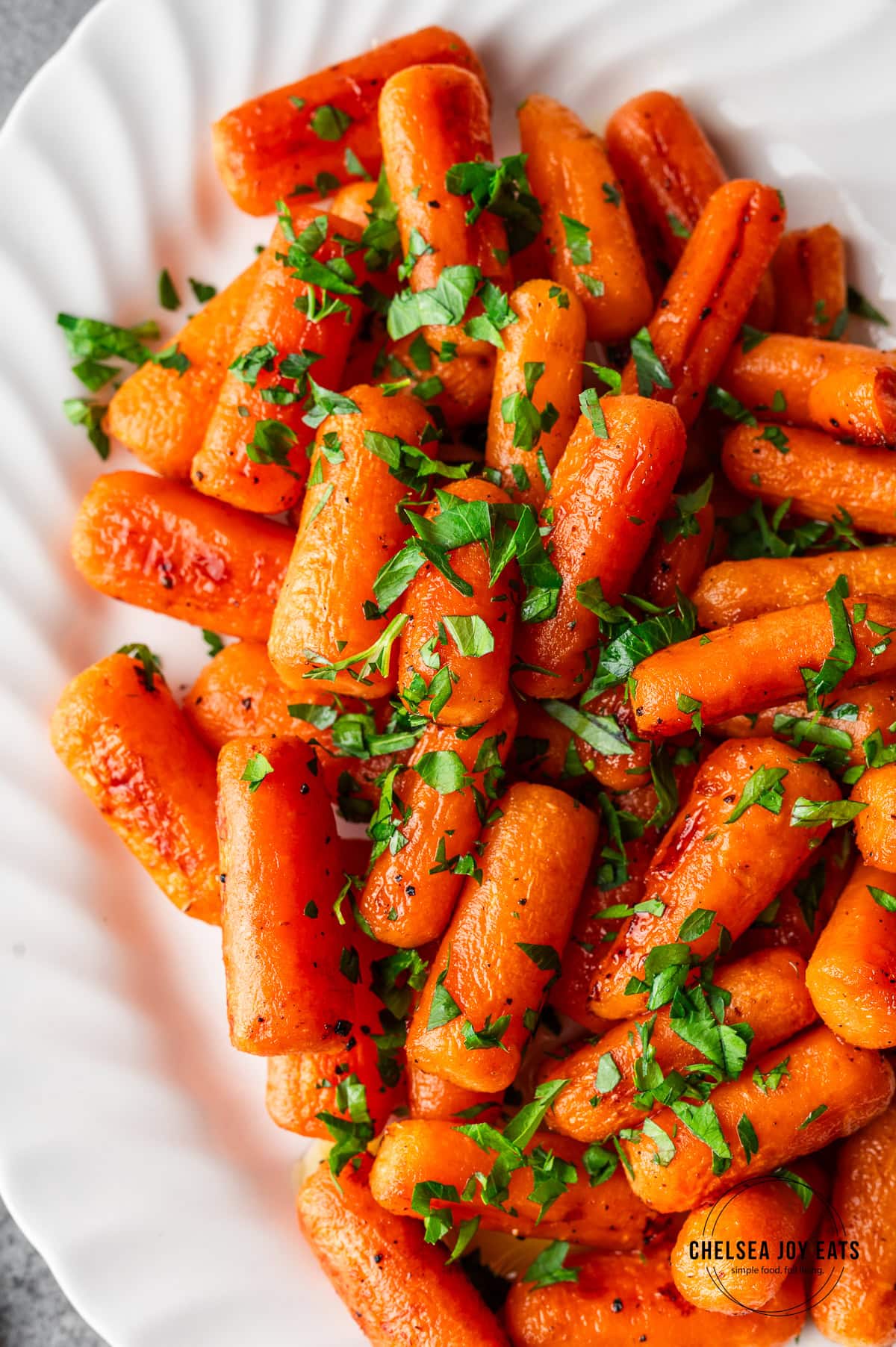 Honey-roasted baby carrots garnished with parsley on a white platter.