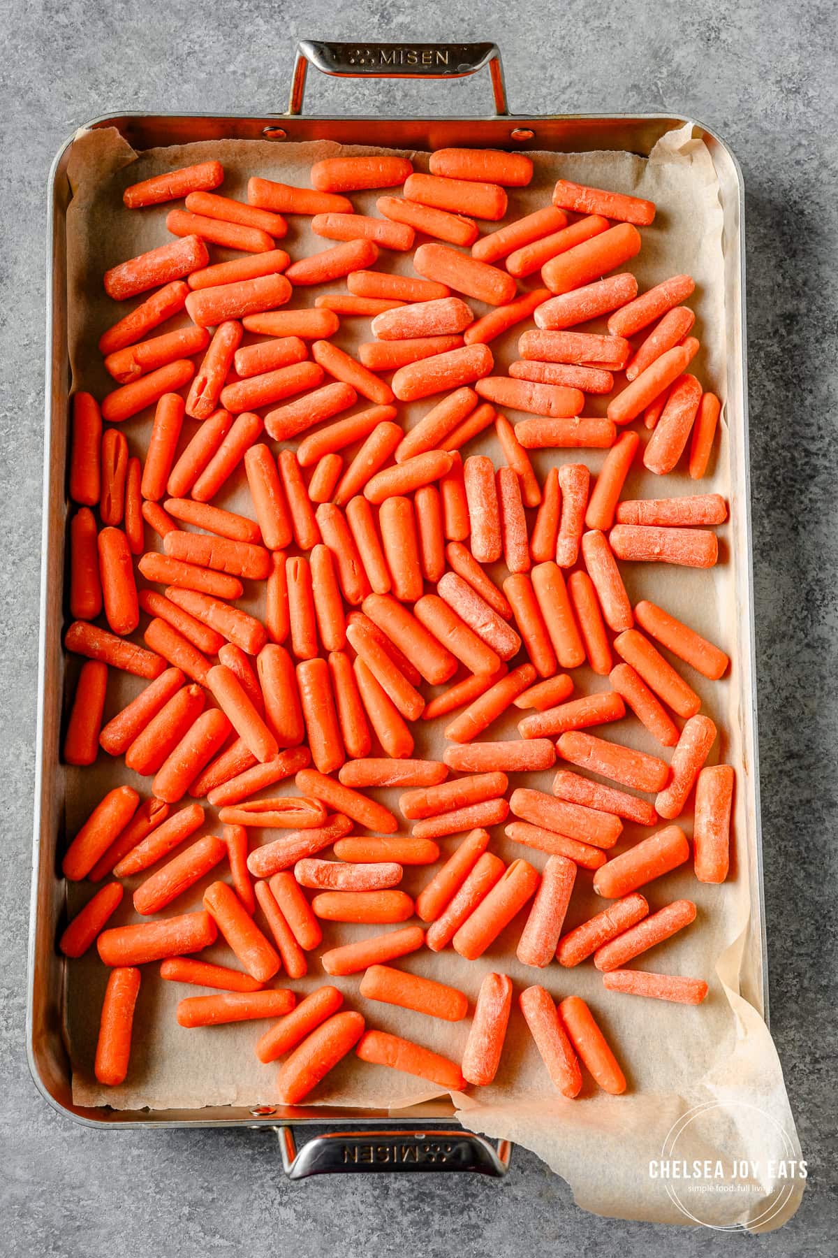 Baby carrots spread out on a parchment paper lined baking sheet.