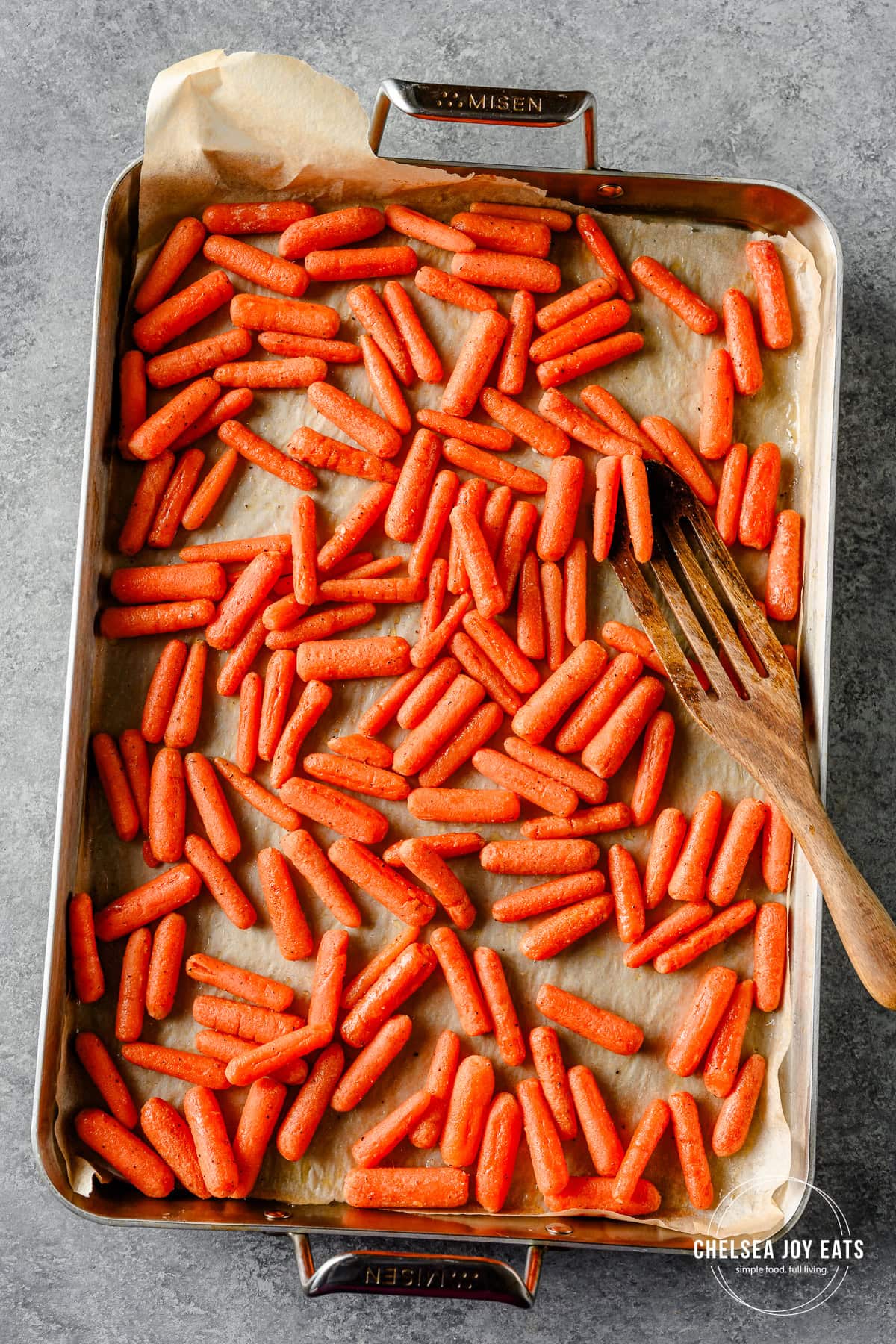 Roasted honey baby carrots with a wooden spatula on a baking sheet.